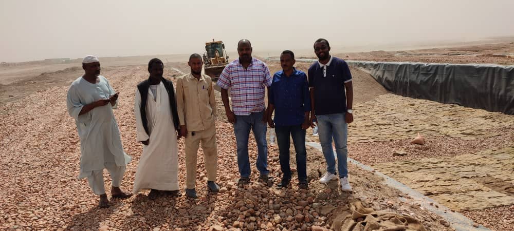 The visiting group beside a lined pond at the site.